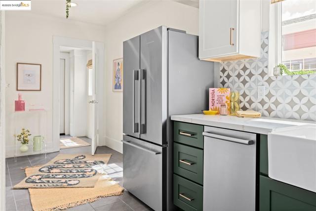 Kitchen with decorative backsplash, green cabinetry, appliances with stainless steel finishes, light stone countertops, and light tile patterned floors