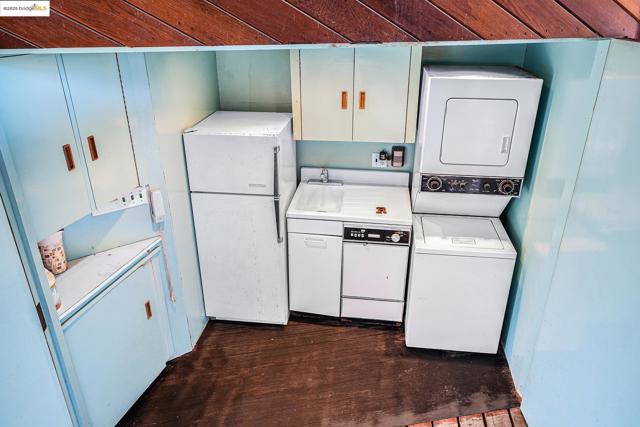 Kitchen with stacked washer / dryer, freestanding refrigerator, dark wood finished floors, and light countertops