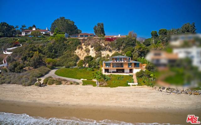 Located in a gated community on a private road, this modern estate designed by architect William Hefner embraces the Malibu lifestyle from the moment you arrive! With 88 feet of beach frontage, its envious location is steps from the beach and boasts 180 views of the ocean from the expansive deck. As you enter through the pivot glass door into the stone foyer with interiors designed by Billy Cotton, the spacious living room draws you in to capture the views as you relax in front of the fireplace. The sliding glass doors open to the expansive deck to enjoy indoor-outdoor living. Experience a one-of-a-kind kitchen equipped with Miele and Gaggenau appliances, floating shelves, a built-in keg, wine fridges, and a large pantry. With skylights overhead, an ocean view breakfast nook and additional island bar seating, sliding glass doors open to a BBQ island, and an outdoor dining area. The owner's suite is a masterpiece spanning the entire top floor for the ultimate privacy. Wood floors and glass walls provide a remarkable backdrop to display your art collection on the built-in shelving throughout the room. The owner's ensuite boasts uncompromising quality with a Toto washlet, freestanding tub, resort-style shower, and stone countertops. The suite is complete with a large closet and a wrap-around balcony. Two additional bedrooms and a media room round out the spaces in this estate. The media room features wood-paneled walls and doors leading to the deck, complete with a lounge area, jacuzzi, additional dining spaces, and heaters, providing everything you need for year-round entertaining. A meticulously landscaped yard with low-maintenance succulents provides year-round beauty to enhance the outdoor spaces. In addition, to a two-car garage, guest park area, and gated entry, the home is equipped with security cameras on the property, a full-house alarm system, and a built-in sound system. This Malibu estate is beautifully appointed with attention to detail and offers exquisite living for the discerning buyer. Schedule your private tour today.