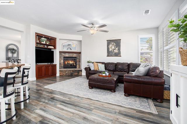 Living room with wood finished floors, raised hearth with a stone fireplace, built-in shelves, and a ceiling fan