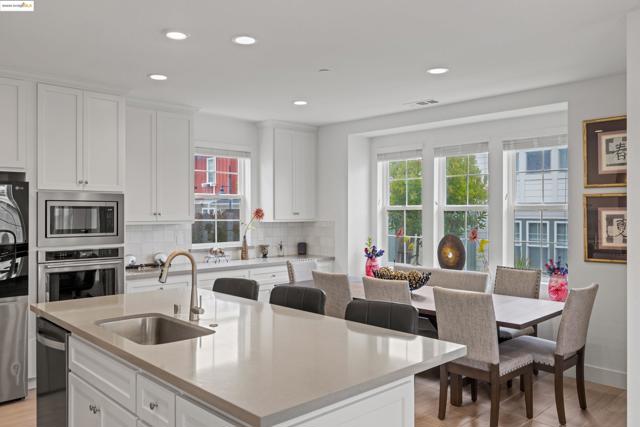 Kitchen featuring white cabinetry, stainless steel appliances, a center island with sink, backsplash, and plenty of natural light