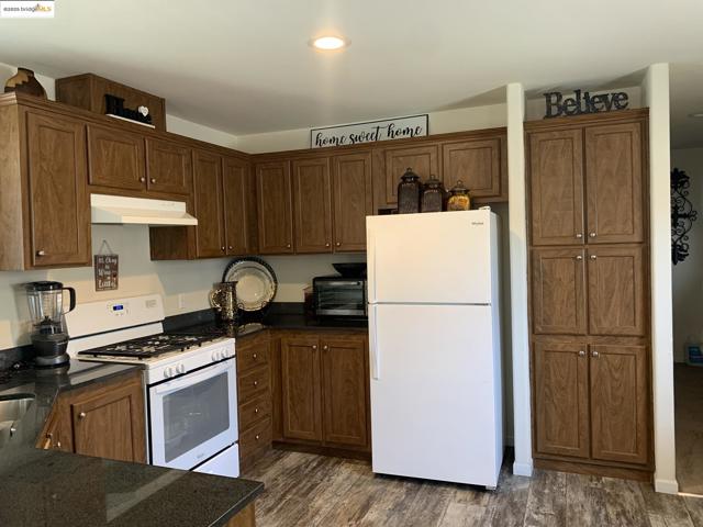 Kitchen with white appliances, dark wood-type flooring, under cabinet range hood, and dark stone countertops
