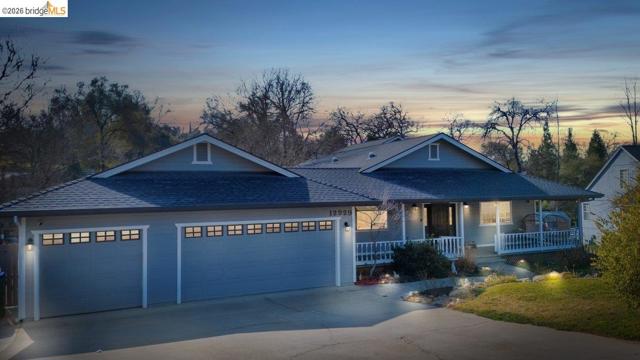 View of front of home with covered porch, driveway, roof with shingles, and an attached garage
