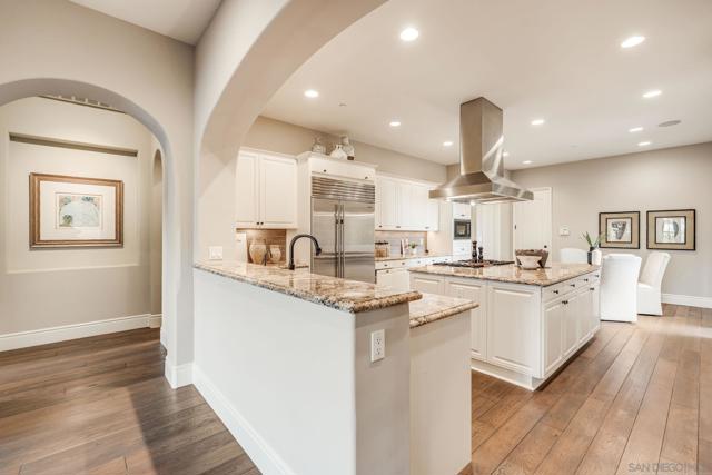 Gourmet kitchen with a spacious island, granite countertops, high-end appliances, and custom cabinetry. Open-concept design flows into the living area, perfect for entertaining. Warm wood flooring and a statement range hood add elegance and functionality.