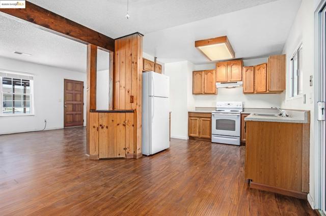 Kitchen with beamed ceiling, white appliances, dark wood-style floors, a textured ceiling, and light countertops