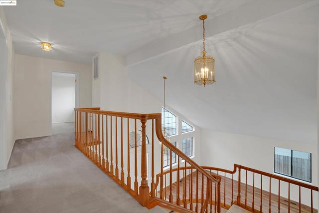 Corridor with light carpet, an upstairs landing, a chandelier, and vaulted ceiling
