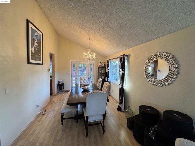 Dining room featuring a textured ceiling, light wood-style flooring, a chandelier, high vaulted ceiling, and a textured wall