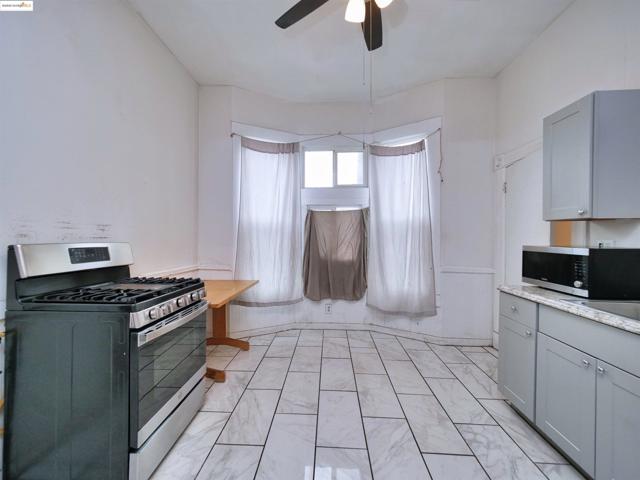 Kitchen featuring stainless steel appliances, gray cabinetry, a ceiling fan, and light stone counters. Virtually staged.
