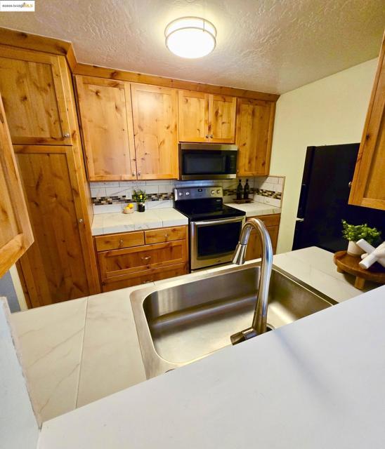 Kitchen with appliances with stainless steel finishes, decorative backsplash, a textured ceiling, brown cabinets, and tile countertops