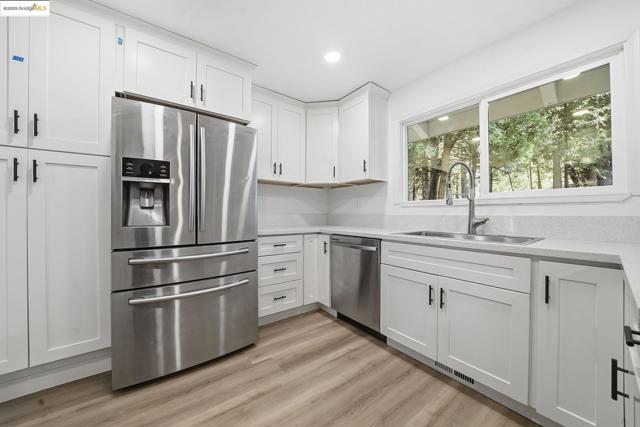 Kitchen with appliances with stainless steel finishes, white cabinets, light wood-type flooring, recessed lighting, and light stone counters