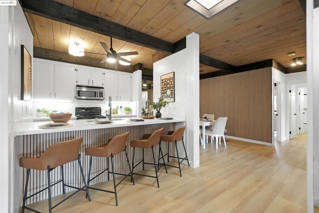 Kitchen with a wooden ceiling with exposed beams, white cabinets, a kitchen breakfast bar, light wood-style floors, and stainless steel microwave