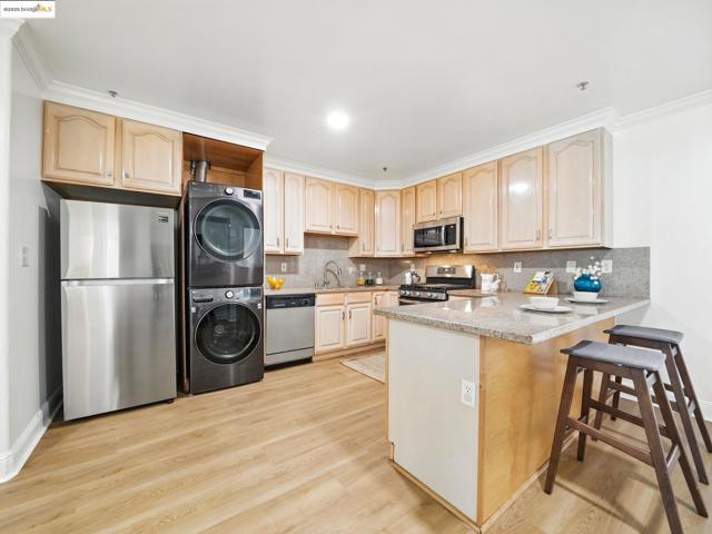 Kitchen featuring stacked washer / dryer, stainless steel appliances, ornamental molding, a peninsula, and light brown cabinets