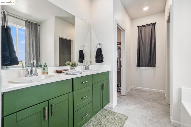 Bathroom featuring double vanity, a garden tub, a spacious closet, and light tile patterned flooring