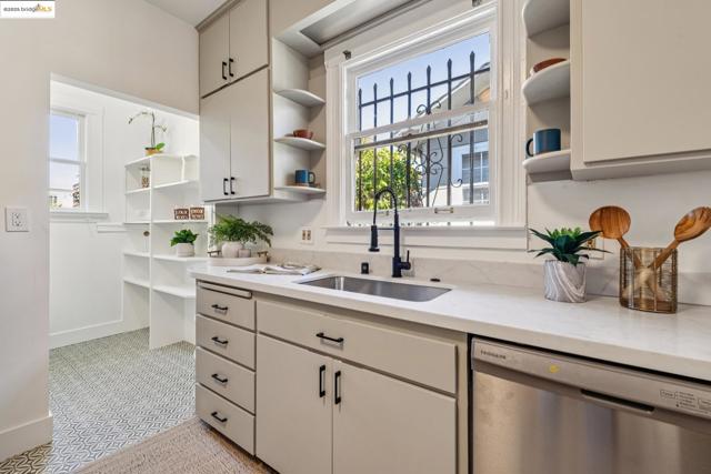 Kitchen featuring open shelves, stainless steel dishwasher, light stone countertops, and cream cabinetry