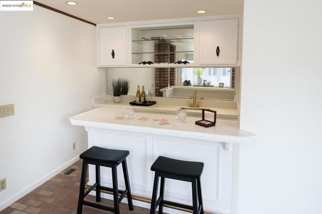 Bar featuring brick flooring, light countertops, white cabinets, recessed lighting, and ornamental molding
