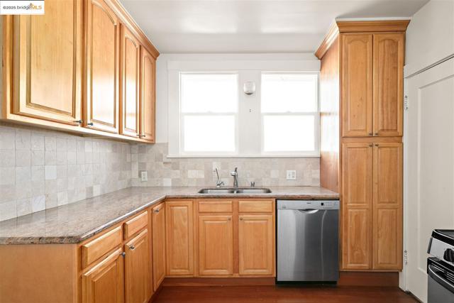 Kitchen with stainless steel dishwasher, light stone countertops, decorative backsplash, dark wood-style floors, and range