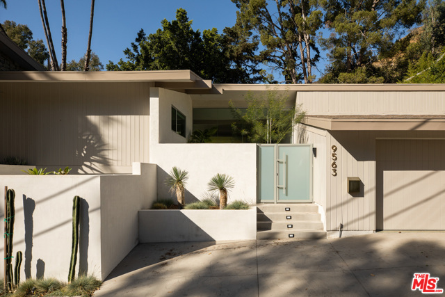 9563 Gloaming Drive Beverly Hills, California Entirely remodeled and expanded architectural gem is a Robert Skinner A.I.A mid century modern on a private street in BHPO. Behind a gated entrance; keeping in-line with the mid century period, stands a pivot door and ridged glass front wall leading to the inviting open floor plan for this 3 bed 4 bath home. The elegant decor brings attention to the restored nods of 1960s design such as the double sided original fireplace anchoring a gracious sunken living room and lounge area both walled in restored wood beams & panels, angled ceilings, & Terrazzo flooring. The bespoke craftsman built bar faces the open dining area and designer kitchen. The primary bed offers a stone fireplace, Amangiri style wet spa and custom cabinetry. The fenced and hedged backyard, reminiscent of a palm springs retreat, invites more than just private enjoyment with a full built in fire-pit, outdoor kitchen and grill and seating, all anchored around a reflecting pool/spa amongst the carefully crafted landscaping.