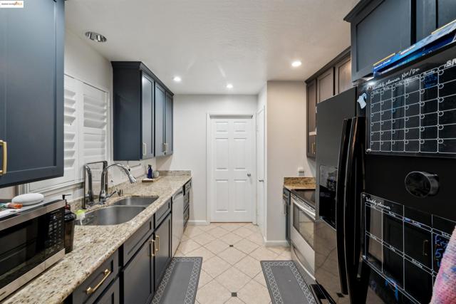 Kitchen with stainless steel appliances, light stone counters, light tile patterned floors, recessed lighting, and dark cabinetry