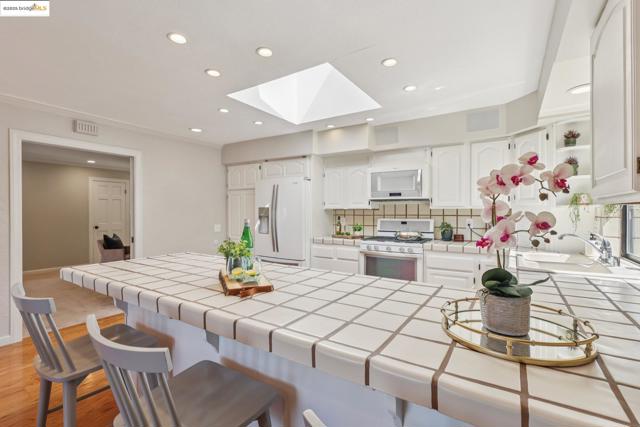 Kitchen featuring tile countertops, a skylight, a breakfast bar, white appliances, and white cabinets