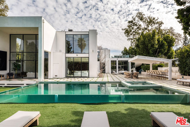Flawlessly executed, an estate of ultimate exclusivity on nearly an acre of privately-gated land, this trophy property was built by architect William Beckett to capture an architectural escape while boasting the most luxurious of amenities and sited in prime Beverly Hills.  Fully reimagined in 2015, large walls of glass bathing the open rooms in natural light, a quintessential wooden curved wall gives a nod to the midcentury architecture and matches the curvature of the exterior grand entrance, and a state-of-the-art chefs kitchen with Miele appliances create a home of functionality and sophistication. A sculptural staircase and lush views from every angle upstairs provide 3 additional secondary bedrooms and the voluminous primary boasting dual closets, a spa-like bathroom with shower, sitting tub, and vanity, an elevator accessing the lower levels, and a private terrace with a hot tub overlooking views of the city. Amenities at scale, the estate was made for both a serene intimate lifestyle and grand gatherings alike, featuring a nail & hair salon, massage room, oversized gym with a view overlooking the backyard terrace, a wine cellar, walk-in safe for additional security, at home theater, and elevator. All rooms of this contemporary 12,000 square foot estate lead to the outdoor oasis with a meditation garden, complete outdoor kitchen with seating, sculpture garden, dual level yard space, a zero-edge infinity pool, a greenhouse, oversized detached garage, and a winding private driveway off this prime Beverly Hills street.