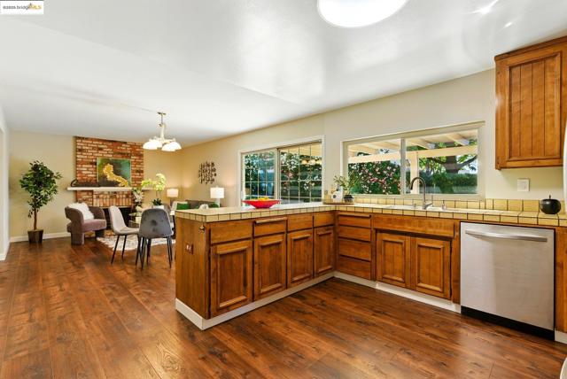 Kitchen featuring brown cabinets, stainless steel dishwasher, dark wood finished floors, a peninsula, and a chandelier