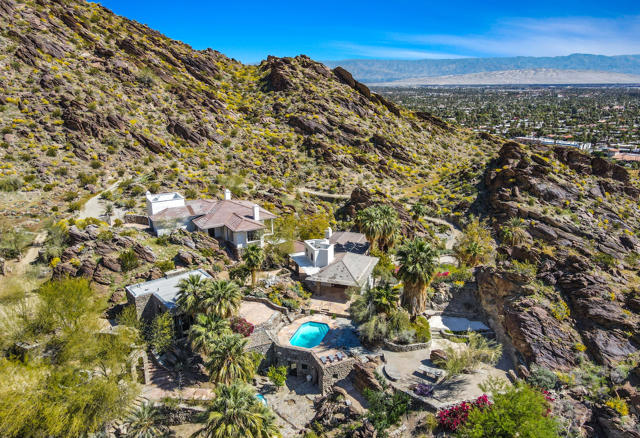 MAGICAL OASIS, The Former home of Suzanne Somers and Alan Hamel. Beyond a discreet gated entrance awaits a hidden paradise that slowly reveals itself, with a meandering driveway leading past a cascading waterfall and landing at a terrace that unveils a European-inspired villa on the hill above. Where a collection of five unique structures unites to create one truly unequaled estate on more than 28 acres of unsurpassed beauty.  Terraced on a hillside naturally embellished with dramatically exposed rock, the estate is both impressive and inviting. An open-air carriage, in the form of a custom funicular, carries passengers up to the residence as panoramic views are revealed below. Intimate walkways, large view terraces and secret patios are interspersed among the buildings, some of which date back 100 years. Explore an outdoor amphitheater, a lagoon-style pool, hiking trails, five world class suites including the Main Suite with its hillside location, heated tub with City views, two offices and terraces and the famous Albert Frey design Rock House. a two-room chef's kitchen with wine cellar, elegant Formal Dining room and poolside Living room. This is the place all will gather for the perfect winter weather and setting. Serene with nature yet minutes to world class dining, entertainment, and Palm Springs International Airport. It is the home you never knew you always wanted.