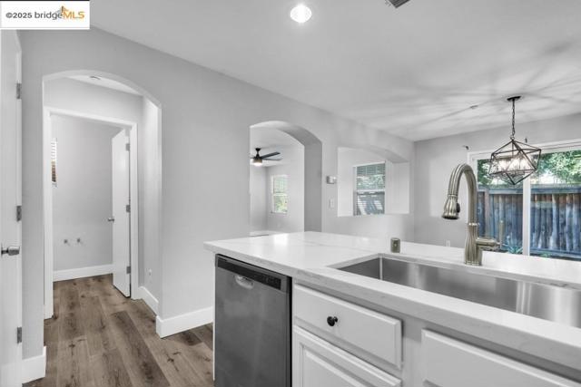 Kitchen with stainless steel dishwasher, wood finished floors, white cabinets, ceiling fan, and light stone counters