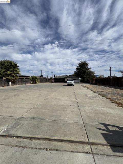 Expansive concrete lot with partial fencing and mature trees