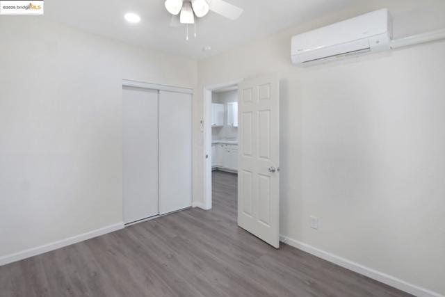 Unfurnished bedroom with a wall mounted air conditioner, wood finished floors, a closet, and a ceiling fan