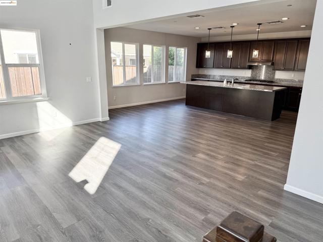 Kitchen featuring dark brown cabinetry, open floor plan, an island with sink, decorative light fixtures, and dark wood-style flooring
