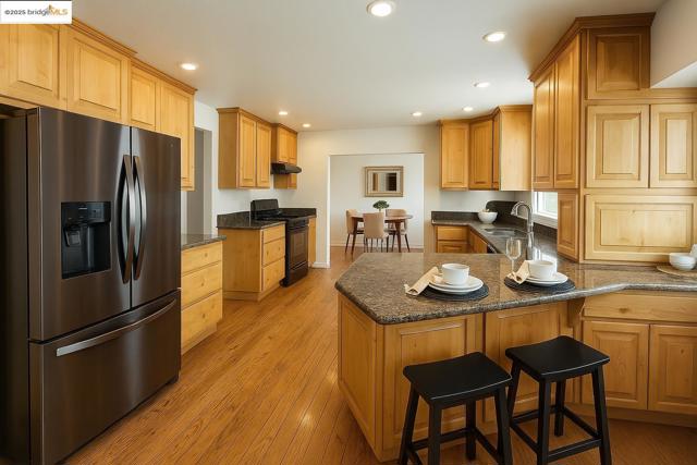 Kitchen featuring stainless steel refrigerator with ice dispenser, a peninsula, black stove, light wood-style floors, and a breakfast bar