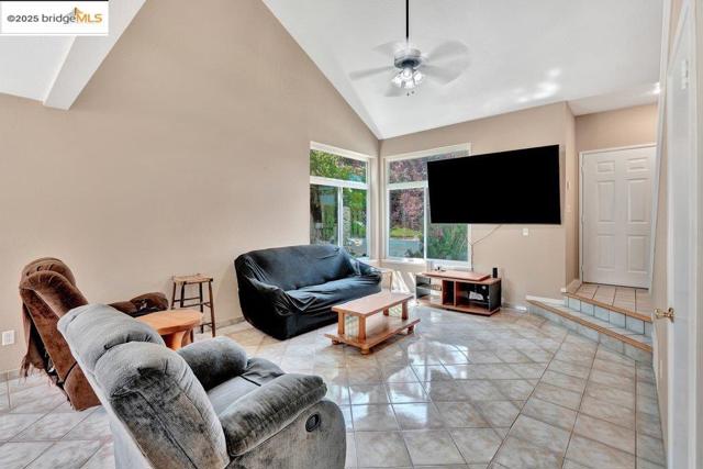 Living room featuring high vaulted ceiling, a ceiling fan, and light tile patterned floors