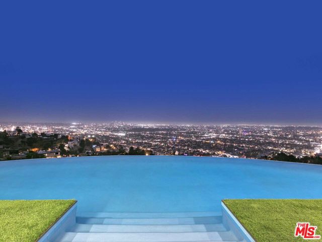 Welcome to this exquisite modern house perched on the hills of the famed Sunset Strip, offering breathtaking views of the city's iconic skyline from downtown to the ocean. This stunning property boasts sleek contemporary architecture, designed to harmoniously blend with its natural surroundings. As you enter inside, you'll be captivated by the open-concept living spaces flooded with natural light, courtesy of expansive floor-to-ceiling windows that frame the picturesque panorama. The main level consists of a formal dining room with a wine cellar, a sleek bar for entertaining, a chef's kitchen with sliding glass doors to an outdoor dining area, and a fireplace made perfect for dining al-fresco. A gym and office complete this magnificent entertaining space. The second level has floor-to-ceiling sliding glass doors that allow access to incredible views of the city and overlooking the infinity pool. A decadent primary suite consists of a large bedroom with a view of the city and pool, a large ensuite bath with dual sinks, and a very special two-story oversized closet. Two guest bedrooms and an additional living area complete this floor. Located minutes above the Sunset Strip, the location and views cannot be beaten. What makes this extraordinary property even more enticing is its unbeatable value. Listed at less than half the initial list price, this is an opportunity to own a piece of Los Angeles luxury at a significantly reduced cost. Experience the epitome of modern living, combining architectural brilliance with mesmerizing cityscapes, all at a price that makes this dream home an irresistible reality.