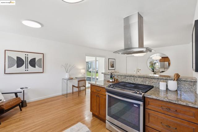 Kitchen with stainless steel gas stove, light stone countertops, light wood-style flooring, brown cabinetry, and island range hood