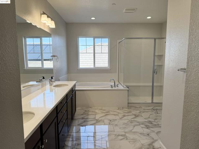 Full bathroom featuring a textured wall, a shower stall, a garden tub, double vanity, and light marble finish flooring