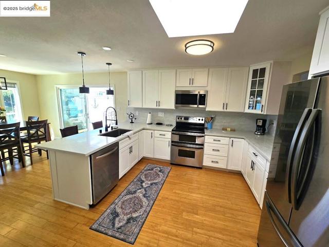 Kitchen featuring stainless steel appliances, white cabinetry, decorative backsplash, and a peninsula