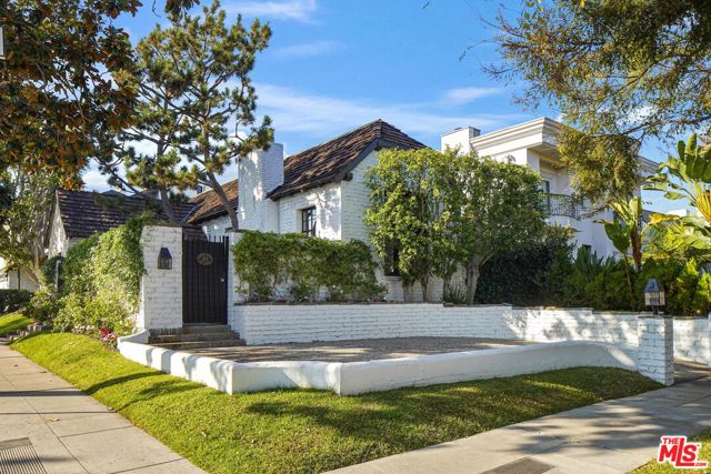 This darling character-rich Beverly Hills cottage is positioned on a corner lot south of Wilshire Boulevard on a desirable tree-lined street. Enter the shaded courtyard via one of two gates to relax amidst the lush greenery. The home's charming pointed arch door welcomes guests inside. The living room features a cathedral ceiling with exposed wood beams, gas stone fireplace, diamond leaded glass window, and French doors opening to the side sunroom perfect for entertaining. The formal dining room has a sliding section door that opens to the beautifully remodeled kitchen, designed by the firm of Cass Calder Smith Architecture, features bar seating, top-of-the-line stainless-steel appliances including Viking Professional range with hood and Miele smart refrigerator, copious cabinetry, eat-in area, skylight, and sliding glass door to the rear patio. There are gleaming wood floors throughout the lower level. Upstairs, the primary suite offers vaulted wood-beam ceilings, fireplace, inlaid shelving for displaying art pieces, comfortable sitting nook, and French door to the private balcony. The main bathroom has a clerestory window bathing the space in natural light, dual-sink vanity, tub, and separate shower. A secondary bedroom has a skylight and loft, and other bedrooms have shutters, wood paneling, and crown moulding. The office accesses the rear patio through a sliding glass door. Outside, dine al-fresco or lounge by the fire pit under the stars. Welcome home!