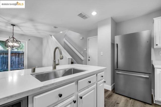 Kitchen with freestanding refrigerator, wood finished floors, white cabinets, hanging light fixtures, and light stone counters