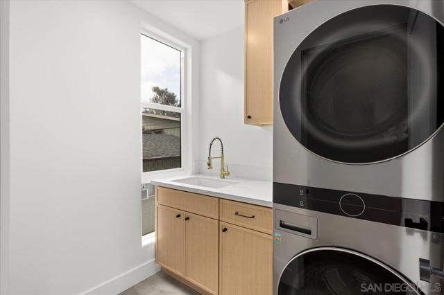 Well lit laundry room with quartz wash station, cabinetry and stackable washer and dryer