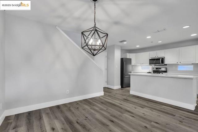 Kitchen with wood finished floors, stainless steel appliances, a chandelier, recessed lighting, and white cabinets