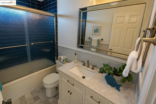 Bathroom featuring bath / shower combo with glass door, vanity, and tasteful backsplash