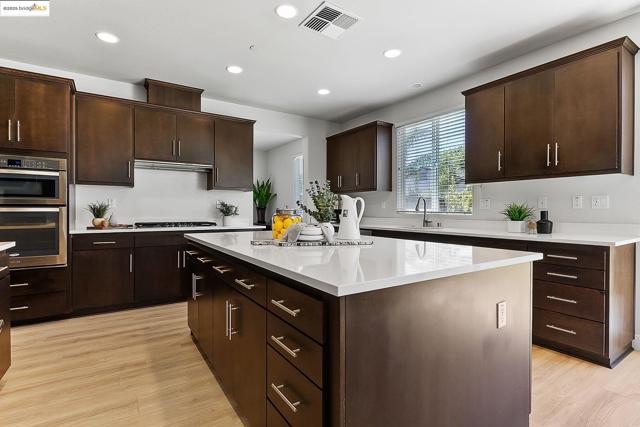 Kitchen with recessed lighting, a kitchen island, stainless steel double oven, light countertops, and dark brown cabinets