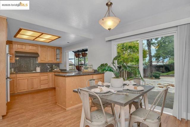 Kitchen with pendant lighting, decorative backsplash, a peninsula, light wood finished floors, and glass insert cabinets