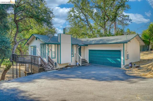 Split-level residence featuring a teal garage door, a front-facing deck with wood railings, and a prominent chimney