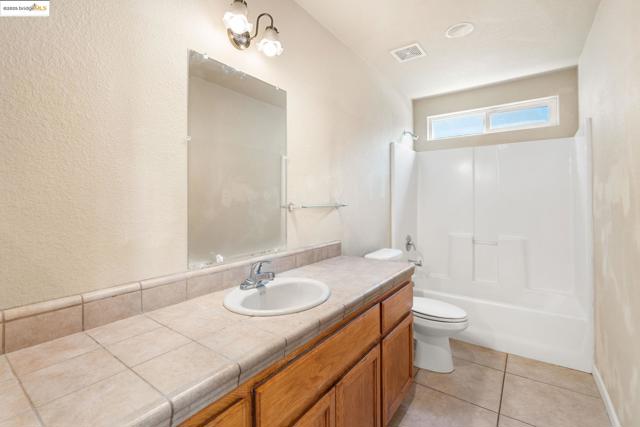 Bathroom with a textured wall, vanity, shower / washtub combination, and light tile patterned flooring