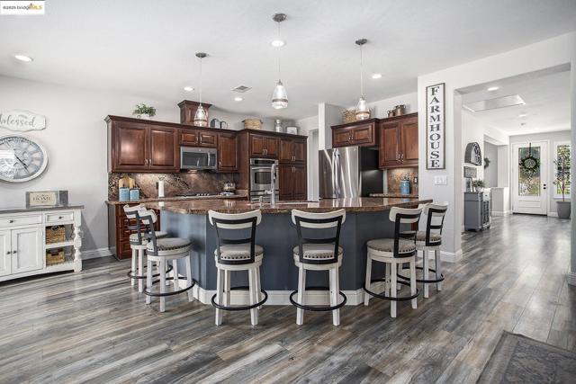 Kitchen featuring tasteful backsplash, dark cabinetry, hanging light fixtures, an island with sink, and recessed lighting