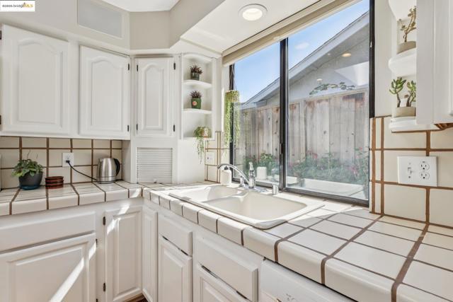 Kitchen with tile counters, white cabinets, decorative backsplash, and open shelves