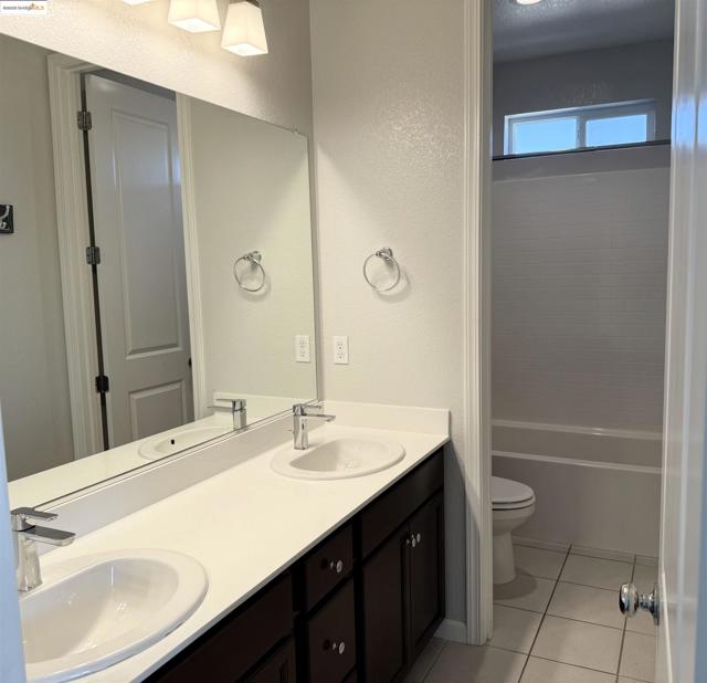 Bathroom with double vanity, light tile patterned flooring, a textured wall, and shower / bath combination