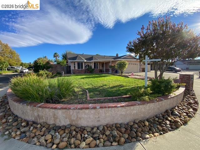 Manicured front lawn with a raised brick and stucco planter, river rock landscaping, and mature trees