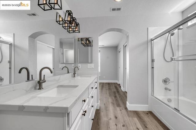 Full bathroom with double vanity, a textured ceiling, wood finished floors, enclosed tub / shower combo, and recessed lighting